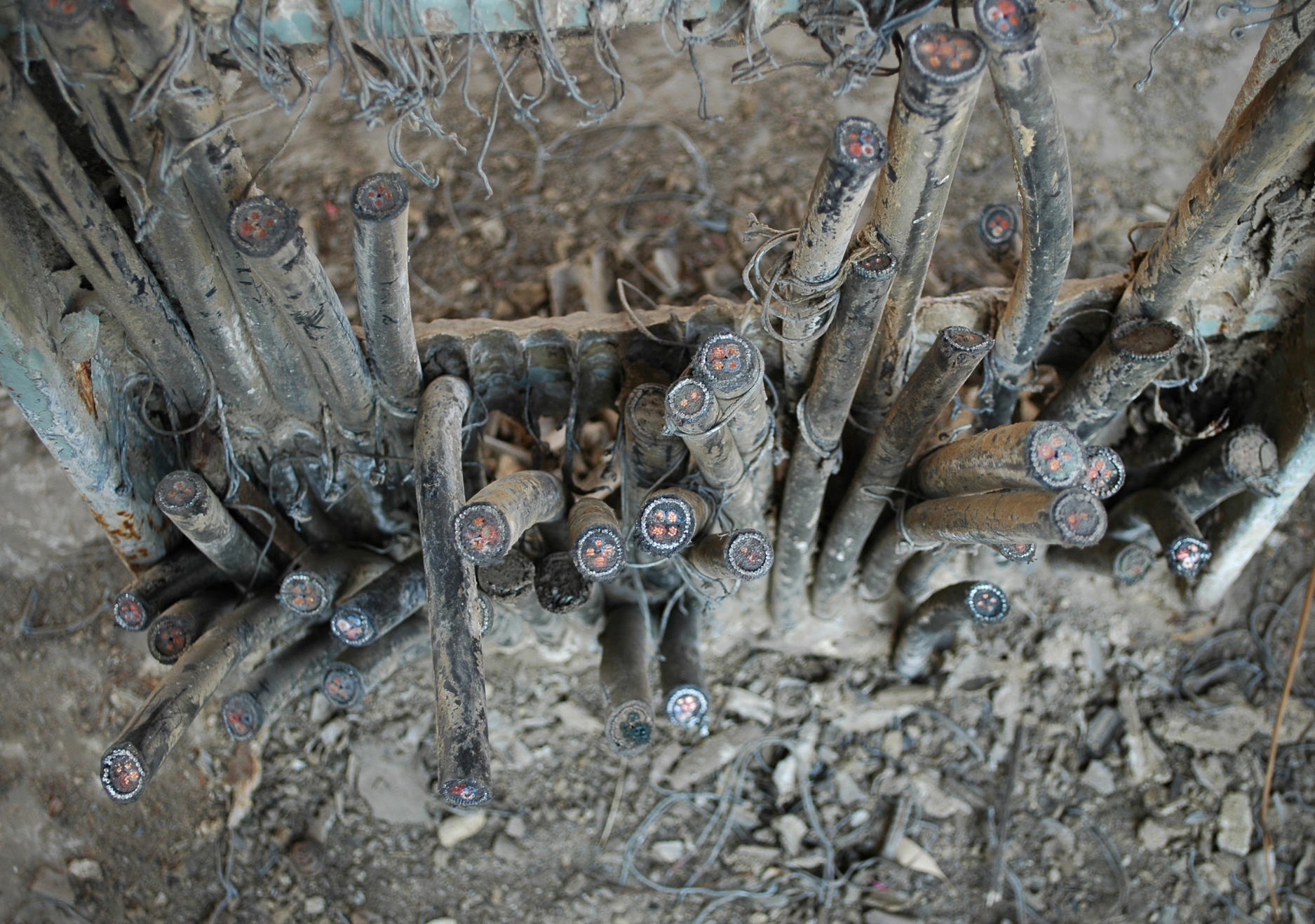 Close-up of dusty electrical cables with exposed ends and red cores, tangled among dirt and debris.