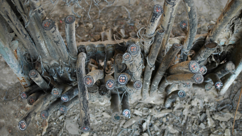 Close-up of dusty electrical cables with exposed ends and red cores, tangled among dirt and debris.
