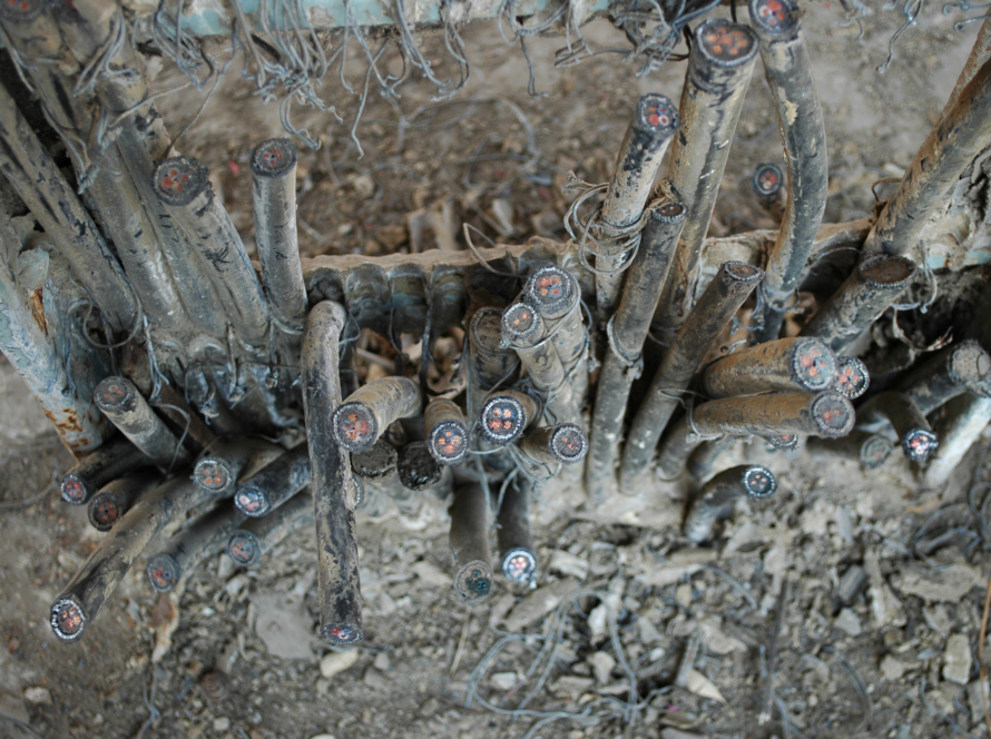 Close-up of dusty electrical cables with exposed ends and red cores, tangled among dirt and debris.